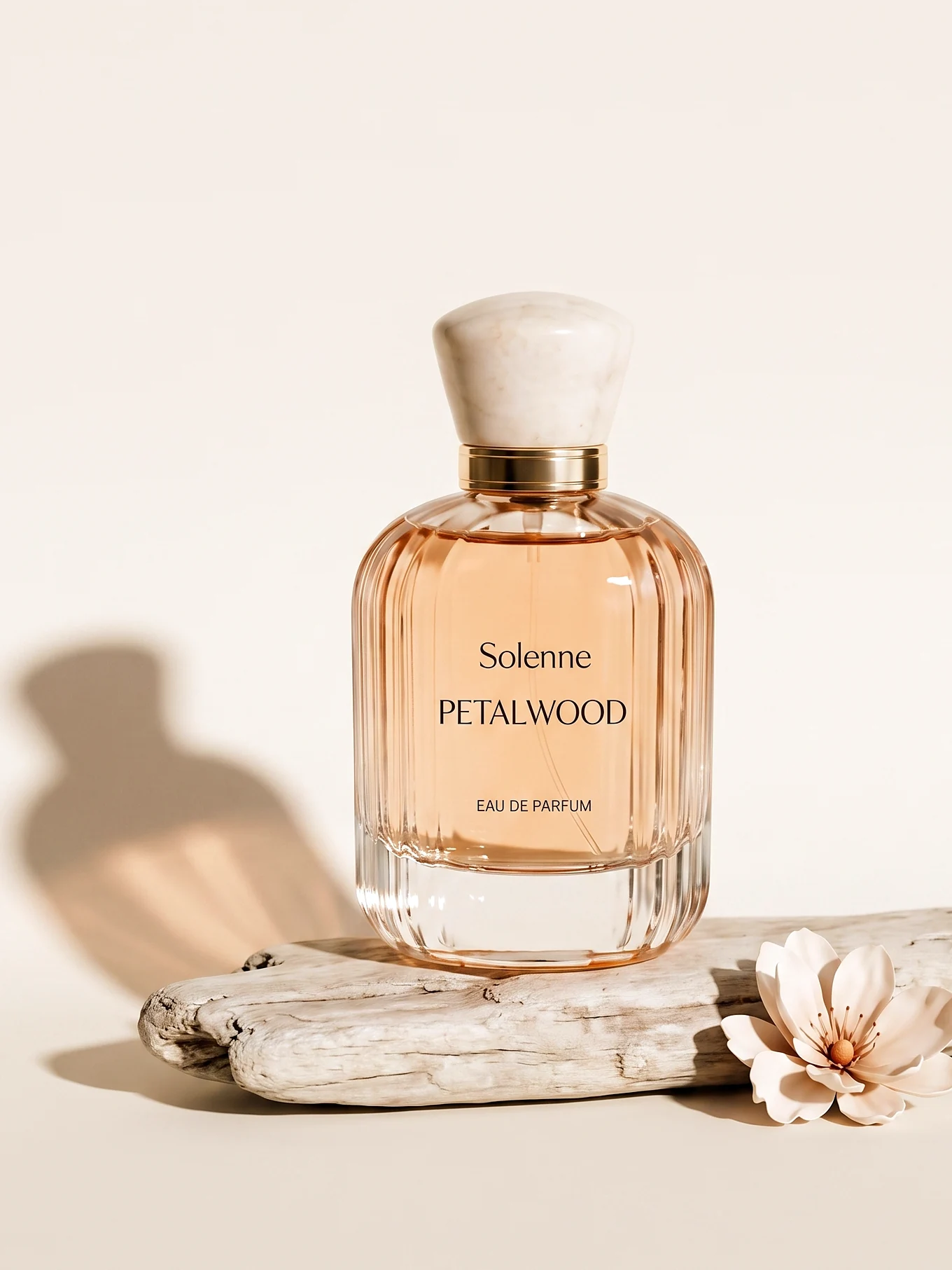 The Petalwood eau de parfum on a driftwood plinth beside a magnolia blossom.